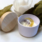 Candle in a white bowl with a wooden lid, surrounded by white flowers on a light background, with 'Mystical Moon' text. handmade unique candle with keepsake moon necklace pendant made in canada