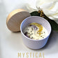 Candle in a white bowl with a wooden lid, surrounded by white flowers on a light background, with 'Mystical Moon' text. handmade unique candle with keepsake moon necklace pendant made in canada