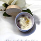 Candle in a white bowl with a wooden lid, surrounded by white flowers on a light background, with 'Mystical Moon' text. handmade unique candle with keepsake moon necklace pendant made in canada
